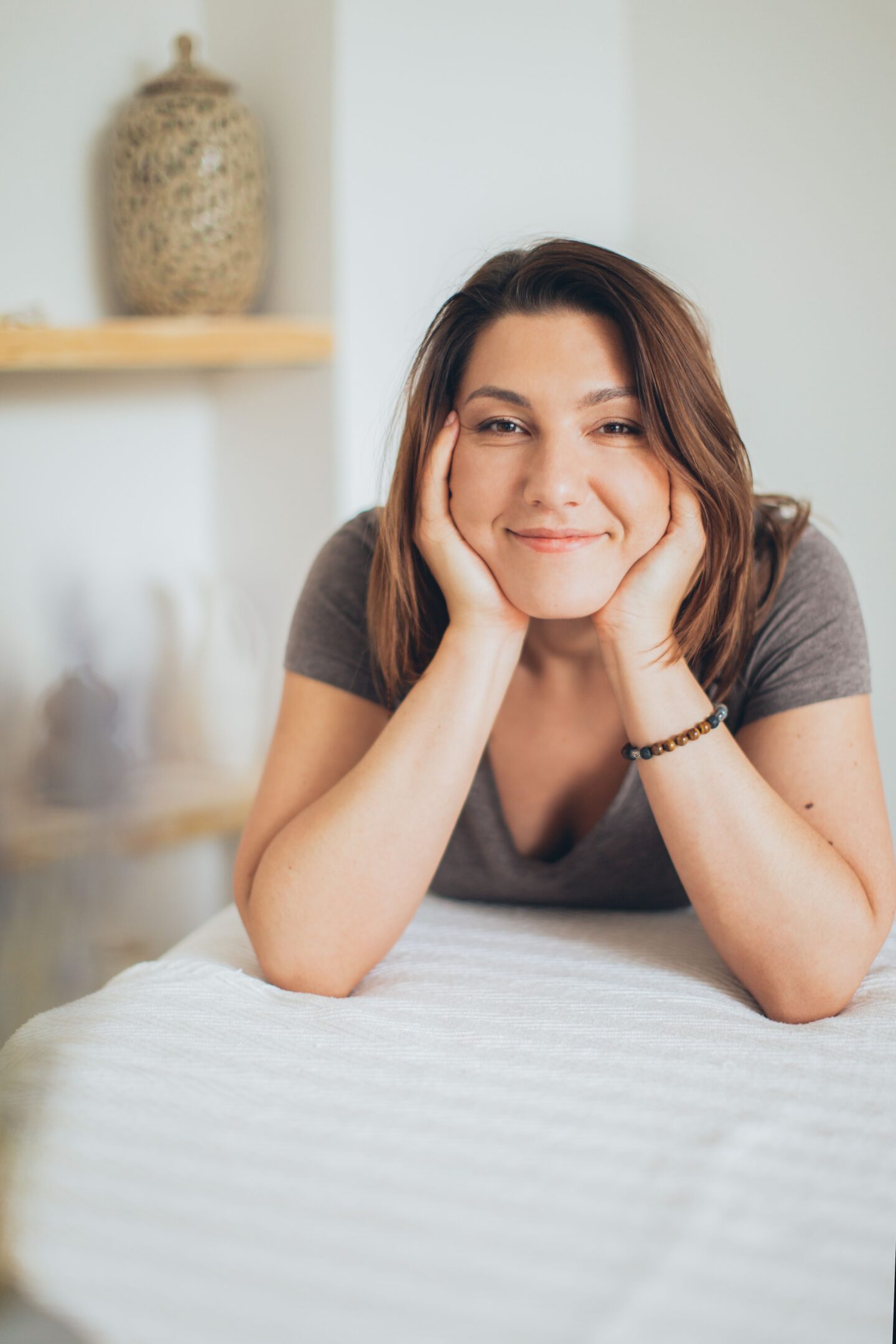 A woman resting her chin on her hands, smiling softly in a calm room