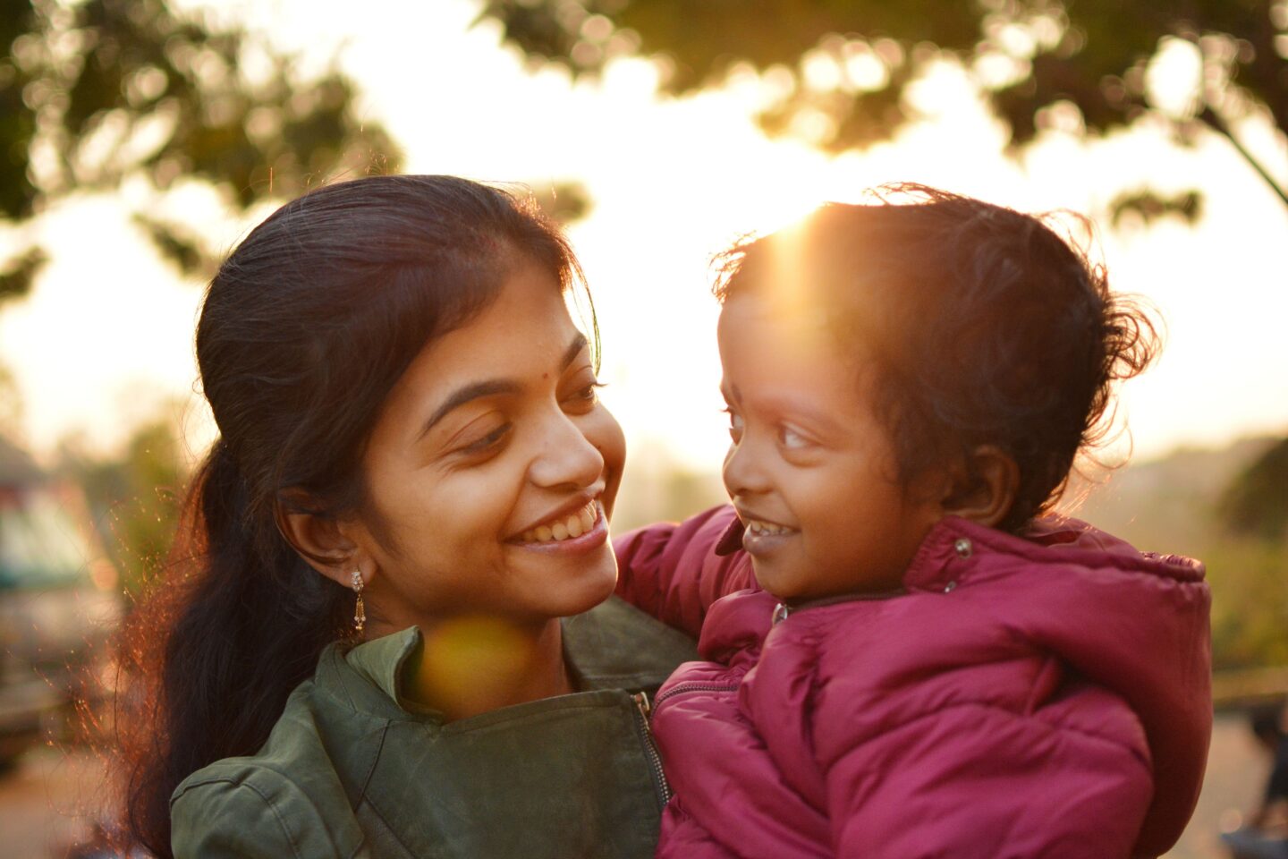 A parent and child smiling face to face at golden hour