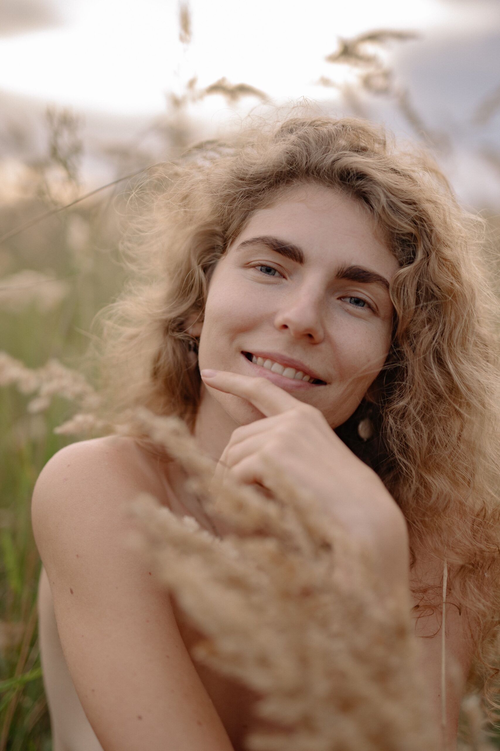 A woman smiling softly in a sunlit field of tall grass
